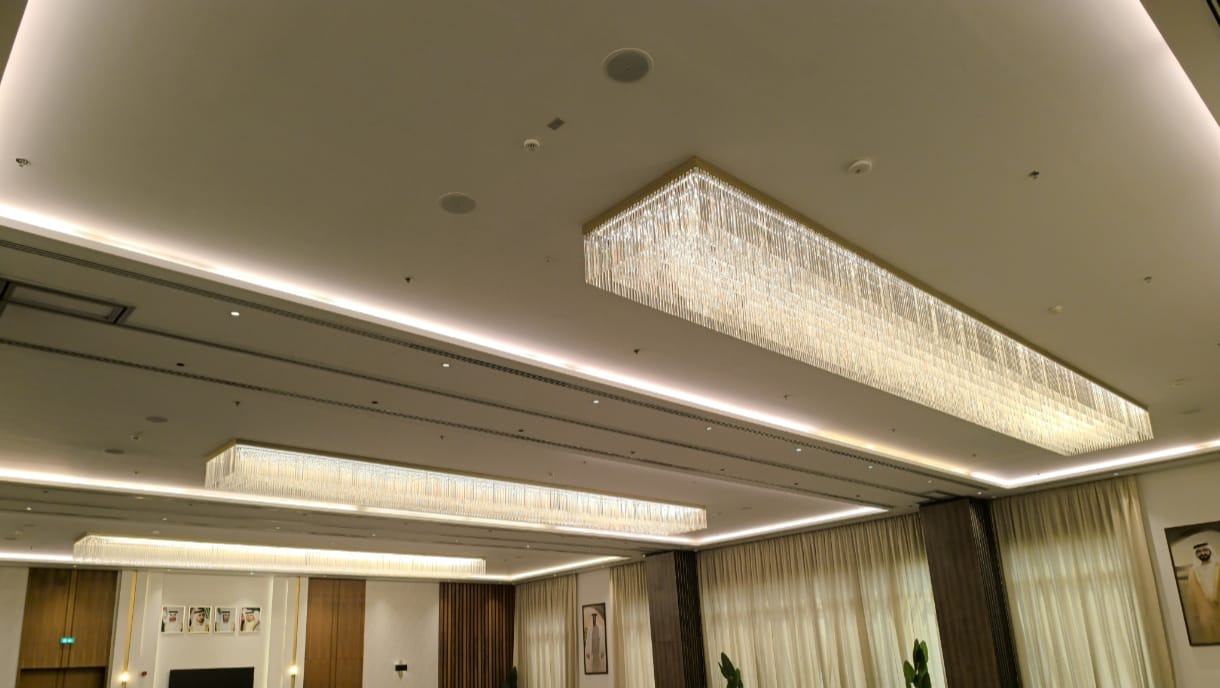 Three linear crystal chandeliers lit in the finished majlis, the largest set into a recessed ceiling panel