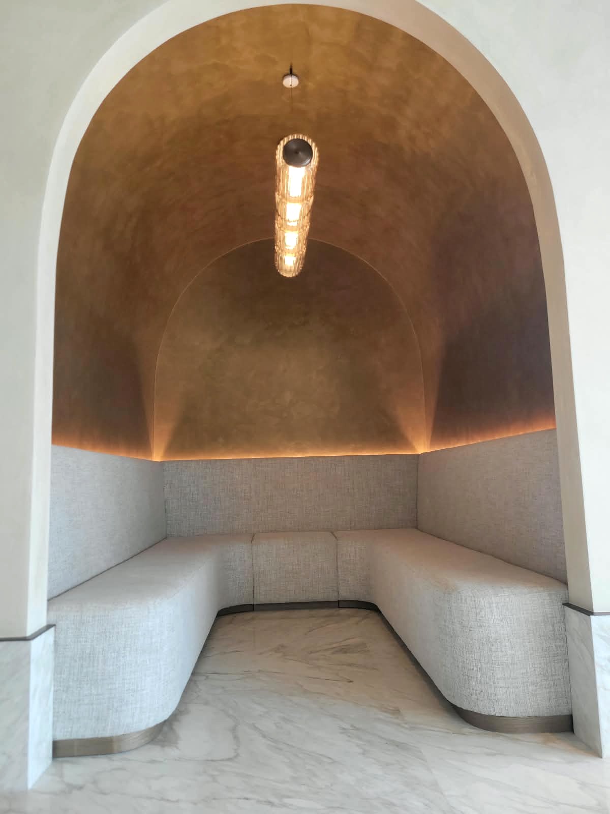 Vertical stack of fluted glass modules lit inside a bronze plaster arched alcove above a curved banquette