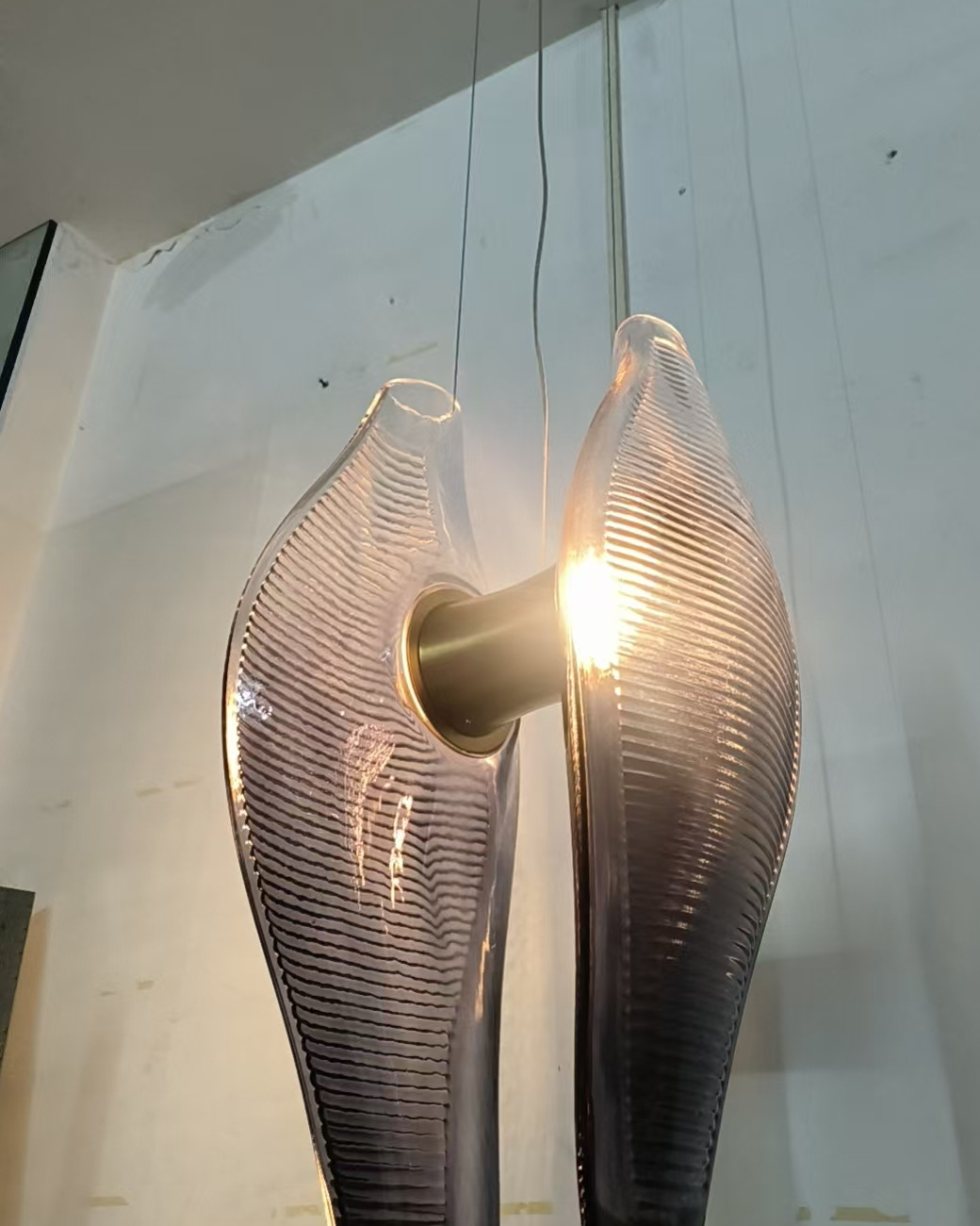 One chandelier unit hung and lit at production, two ridged glass shells on a brass-tone core