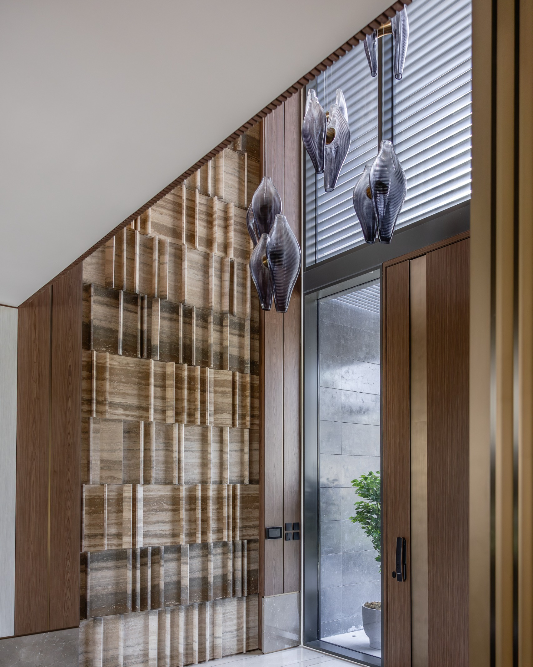 Glass chandelier of paired smoky grey ribbed shells suspended through a double-height villa entrance